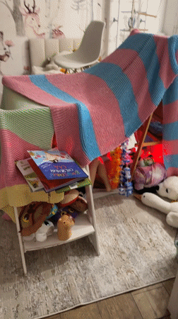 Child plays in illuminated blanket fort with stuffed animals