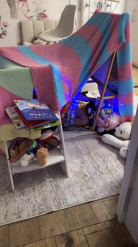 Child plays in illuminated blanket fort with stuffed animals