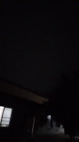 A very dark, blurry video shows a faint light in the bottom left corner, possibly a window. The rest of the scene is indistinct, appearing to be an interior space with dark walls and a ceiling. There is a horizontal element visible near the top that might be a beam or shelf. The video appears to capture a person's perspective, as if they are looking around the room. The lighting conditions are extremely poor, suggesting it is nighttime or a very dark interior. The majority of the video is black, indicating very little light is present.