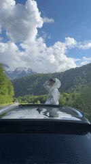 Person stands through car sunroof, shields eyes in Estosadok