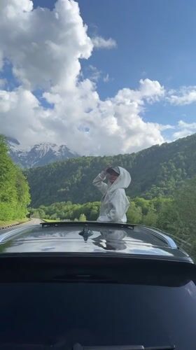 Person stands through car sunroof, shields eyes in Estosadok