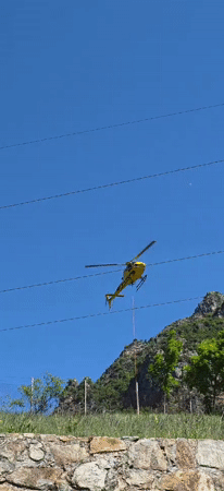 Yellow helicopter with suspended rope flies near powerlines in Spain