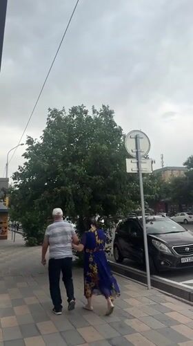 Pedestrians walk on checkered sidewalk in cloudy Tashkent
