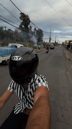 Motorcyclist rides red scooter through Mengwi street