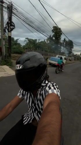 Motorcyclist rides red scooter through Mengwi street