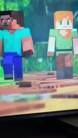 The video shows two Minecraft characters, Steve and Alex, walking through a forest biome. Steve is on the left, wearing a blue shirt and purple pants. Alex is on the right, wearing a green shirt and brown pants and holding a trident. The environment is lush with green trees and foliage, with a path made of dirt and wood planks. The camera pans to show a serene landscape with a pond, bamboo, and stone blocks.