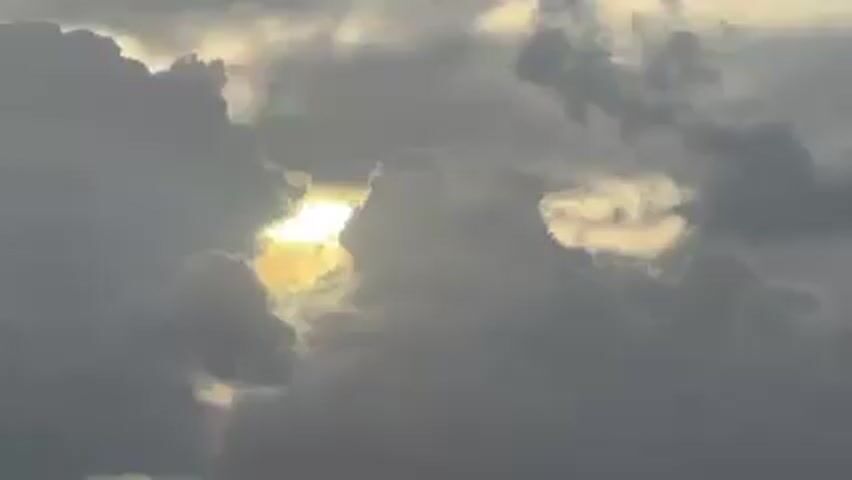The video shows a view of the ocean on a cloudy day. The sun is partially obscured by clouds, but its rays are shining through in beams. The water is choppy, with small waves breaking on the surface.