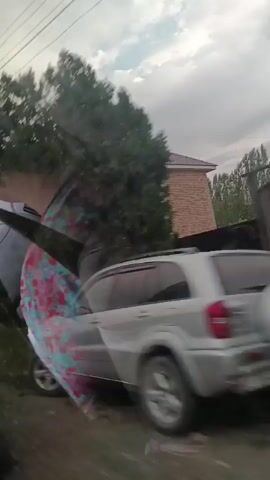 The video shows a moving shot of a residential area with a brick house and trees. A utility pole with wires is visible. The shot appears to be taken from a vehicle. The weather is overcast.