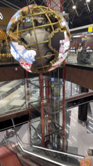 Two people use escalator beneath digital globe display in Russia
