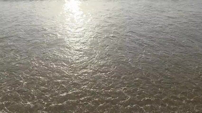 The video shows a beach with waves rolling onto the sand. The sun is shining and reflecting off the water. The waves are gentle and create a calming atmosphere. The sand appears to be light brown in color. There are no people or objects visible in the video. The camera is positioned at a low angle, looking out towards the ocean. The overall impression is one of peace and tranquility.