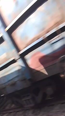 The video shows a train car moving quickly past the camera. The train car is blue and gray with rust stains. The railroad tracks are visible below.