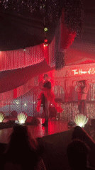 Two performers on a silver-curtained stage lit in red and pink