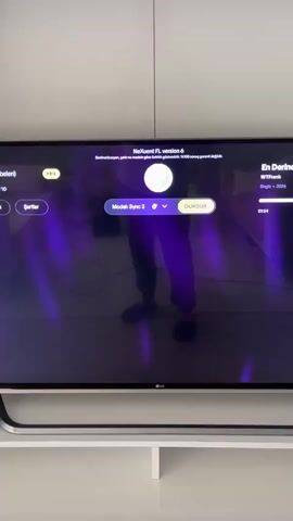 The video shows a television screen displaying a karaoke interface. The screen is dominated by a dark background with purple and blue light streaks, suggesting a stage or performance setting. In the center of the screen, a person's silhouette is visible, standing in front of the TV.

The karaoke interface has several text elements. At the top, it reads "Nexuett FL version 6". Below that, in smaller text, it says "Senkronizasyon, şarkı ve modülasyon gizli farklılık gösterebilir. %100 sonuç garanti değildir." On the right side, song information is displayed: "En Derine" by "WTFrank", with "Single - 2026" and a timestamp of "01:55". In the center, there are control buttons. One button says "Şartlar", another says "Model: Sync 2" with a dropdown arrow, and a prominent yellow button says "DURDUR" (which means "Stop" in Turkish).

Below the control interface, lyrics are displayed in white text. The first line is "Aaah geçmişime", followed by "Küle döndüm resmimize". The lighting suggests the video was recorded indoors, likely in a living room or entertainment space, given the presence of a TV stand. The time of day is not discernible. The overall mood is that of a casual entertainment session, possibly a karaoke night. The song appears to be in Turkish. The location context provided is Gürsu, Turkey, which aligns with the Turkish lyrics.