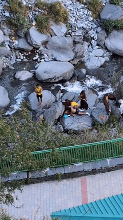 Monks and visitors gather at rocky riverbed in Bhagsu