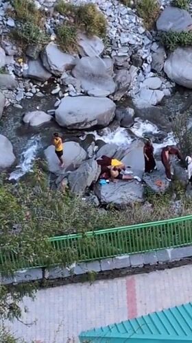 Monks and visitors gather at rocky riverbed in Bhagsu