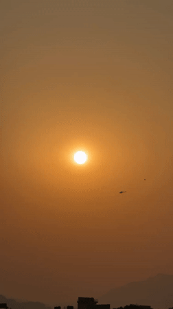 Helicopter flies through hazy sunrise skies over Pokhara, Nepal