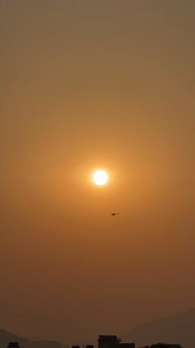 Helicopter flies through hazy sunrise skies over Pokhara, Nepal