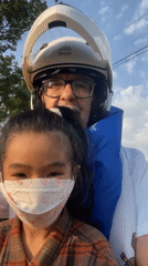 Man and girl ride motorcycle in Vietnam, girl flashes peace sign