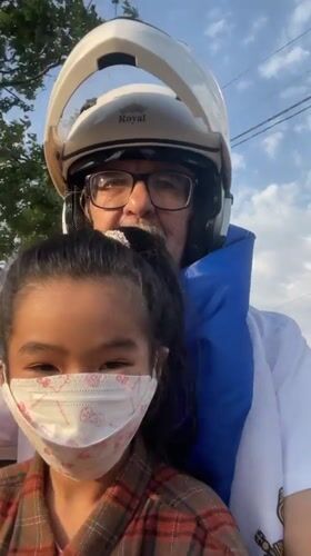 Man and girl ride motorcycle in Vietnam, girl flashes peace sign