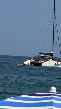 Packed summer beach day in Badalona, catamaran anchored offshore