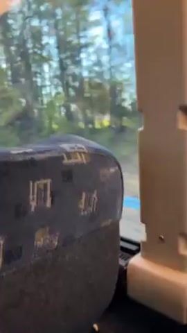 The video shows the interior of a bus or train, focusing on a seat with a patterned fabric. Outside the window, trees and foliage are visible, suggesting the vehicle is moving. The overall impression is of a view from inside public transportation during transit through a wooded area.