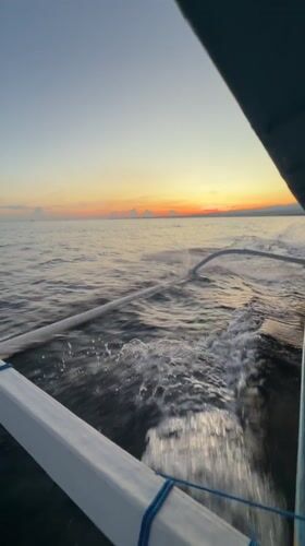 Boat crosses Bali waters at sunset near industrial coastline