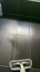 Person cleans black tiled floor with flat mop