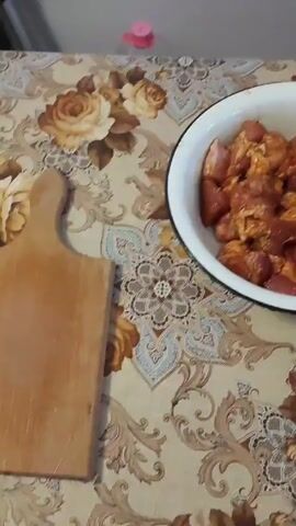 The video shows a white bowl filled with chunks of raw meat. The meat appears to be coated with spices or a marinade. The bowl is sitting on a tablecloth with a floral pattern. A wooden cutting board and a plastic bottle are visible in the background. The camera zooms in on the meat, providing a closer view of its texture and color. The audio consists of upbeat music.