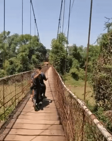 Motorcycle riders cross wooden suspension bridge in Battambang