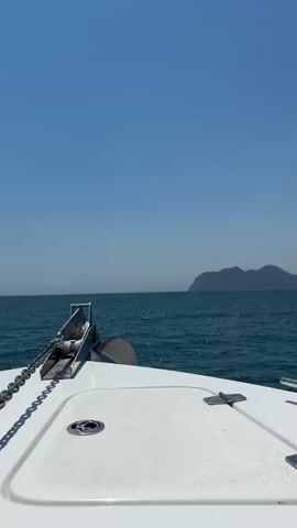 This video captures a serene moment at sea, with the camera positioned on the bow of a white boat. The main subject is the boat itself, specifically its anchor and chain, prominently displayed in the foreground. Beyond the boat, the vast expanse of the turquoise sea stretches to the horizon, meeting a clear, bright blue sky. In the distance, a hazy, mountainous landmass is visible, suggesting a coastal location.

The activity taking place is a boat journey on a calm sea. The gentle movement of the water indicates the boat is either cruising or has temporarily stopped. The overall mood is peaceful and tranquil, enhanced by the clear weather and the expansive natural scenery. The time of day appears to be daytime, likely late morning or early afternoon, given the bright sunlight and clear visibility. The location context of Köyceğiz, Turkey, implies this could be a view of the Aegean or Mediterranean coast, or perhaps a large lake if Köyceğiz Lake is being traversed. There is no visible text in the video. The focus is entirely on the natural elements and the boat.