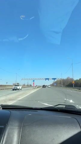 The video shows the dashboard view from inside a car driving on a highway during the day. Overhead road signs indicate directions towards Izhevsk and Perm. The sky is clear and blue. Other vehicles are visible on the highway in the distance. Roadside features include guardrails and evenly spaced lampposts.