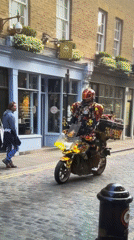 Colorfully dressed motorcyclist rides customized bike through London cobblestone streets