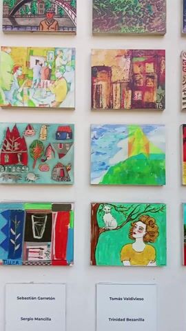The video shows a wall adorned with many small, square paintings or prints. Each artwork is distinct, featuring various subjects, styles, and color palettes. Accompanying each piece is a small label displaying a name, presumably that of the artist. The overall scene suggests an art exhibition or display, likely held in an indoor location.