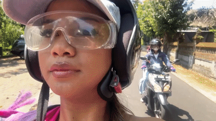 Woman smiles while riding motorcycle in sunny Sukawati