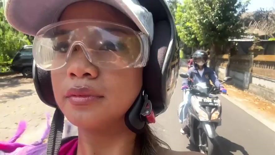 Woman smiles while riding motorcycle in sunny Sukawati