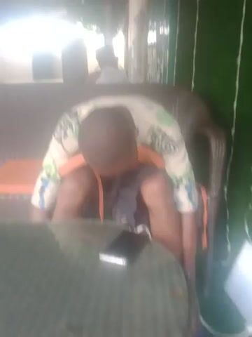 A person is lying down on a chair with a table in front of them. The person is wearing a t-shirt and shorts. A phone is placed on the table.