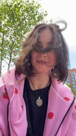 Woman in strawberry hoodie photographed outdoors during windy conditions