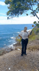 Woman poses on sunny cliffside overlooking ocean