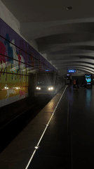 Train arrives at dimly lit subway platform with mural