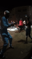 Two men interact on dusty street in Maiburiji