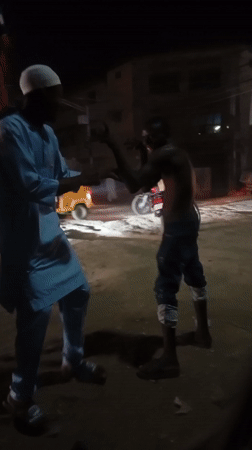 Two men interact on dusty street in Maiburiji