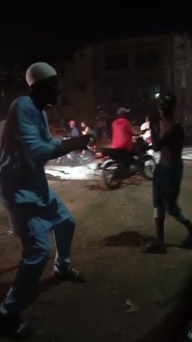 Two men interact on dusty street in Maiburiji