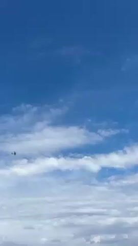 The video shows a small plane flying in a blue sky with puffy white clouds. The camera pans down to reveal a view of the ocean with an island visible in the distance.