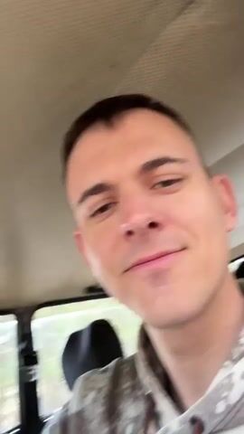 A man is recording a video from inside a car. An Angry Birds plush toy hangs from the rearview mirror. The car stops. A woman exits the car and sits on the hood, holding a tablet. The car appears to be in a forest. The woman waves at the camera.