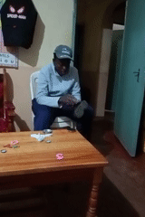 Man polishes boots while child plays at table in Kenya