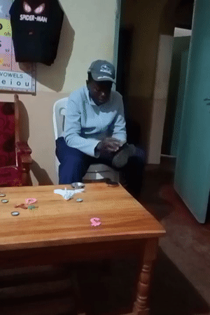 Man polishes boots while child plays at table in Kenya