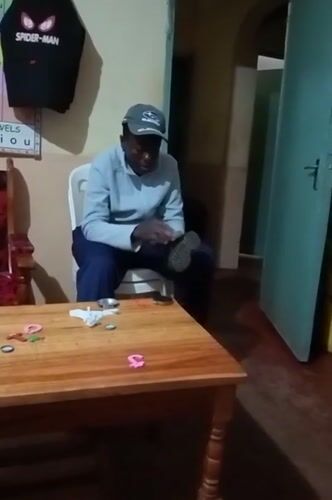 Man polishes boots while child plays at table in Kenya