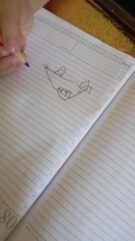 The video shows a person's hand holding a pen and drawing in an open notebook. The notebook has lined pages. The drawing appears to be of an airplane with numbers and lines around it. The background is blurred, but it seems to be a table with a textured surface. The lighting is dim, and the focus shifts throughout the video.