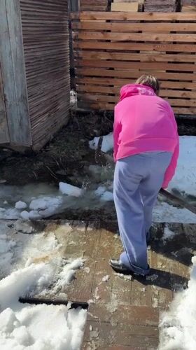 Person shovels snow on wooden deck in Zheleznodorozhny, Russia