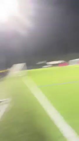 The video shows a soccer field at night, lit by stadium lights. Several players, some wearing pink jerseys and at least one in purple, are dispersed across the green artificial turf. A soccer goal is visible in the background. The camera is relatively static, providing a view of the players and the field's layout.